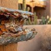 Rusted burst galvanized water pipe leaking at desert stucco home, severe corrosion with dripping water.