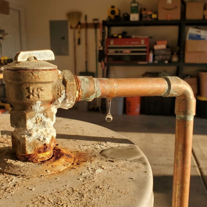 Leaking water heater T&P pressure relief valve, corroded copper pipe with rust and drip in garage.