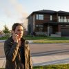 Concerned woman calling 911 as smoke from house fire rises; fire trucks respond in suburban neighborhood.