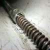Close-up of rusty drain snake auger inside PVC pipe, showing metal coil and debris from plumbing clog removal.