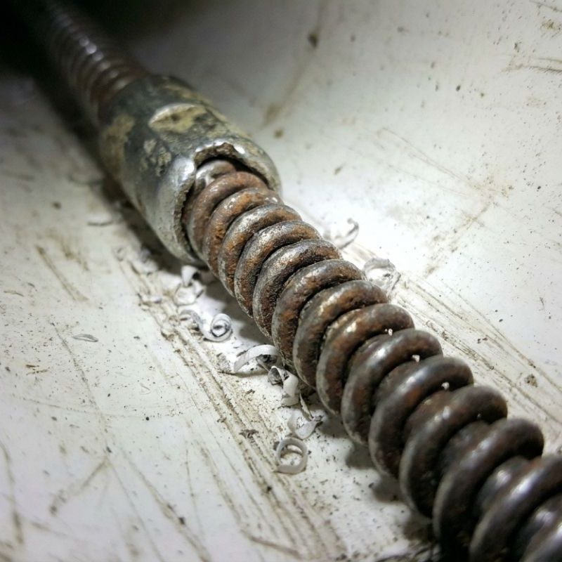 Close-up of rusty drain snake auger inside PVC pipe, showing metal coil and debris from plumbing clog removal.