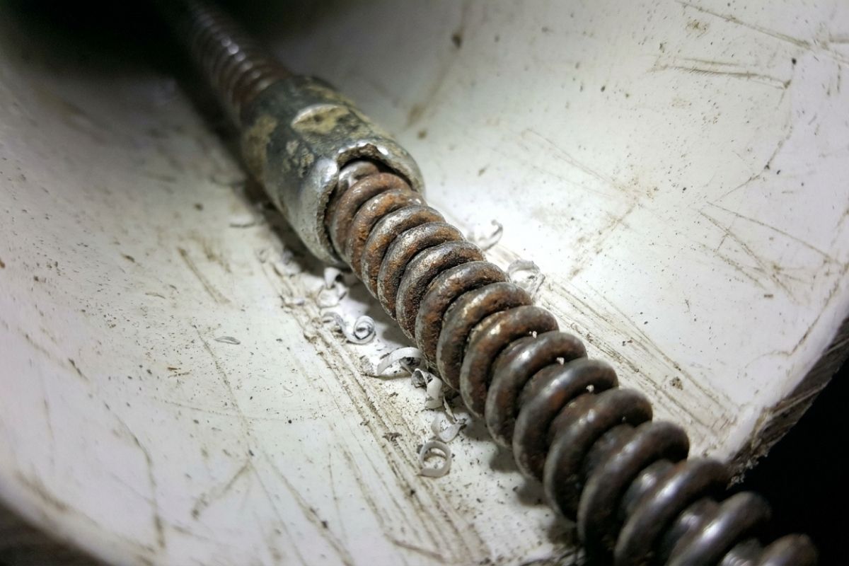 Close-up of rusty drain snake auger inside PVC pipe, showing metal coil and debris from plumbing clog removal.